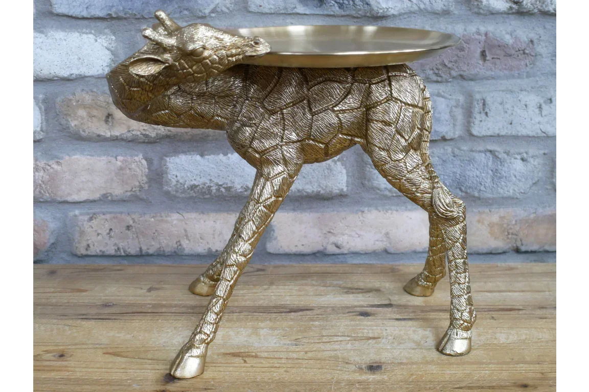 Gold giraffe side table with textured legs and round tray top against brick wall