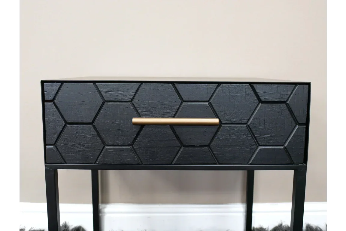Black bedside table with hexagon drawer pattern and gold handle on slim metal legs