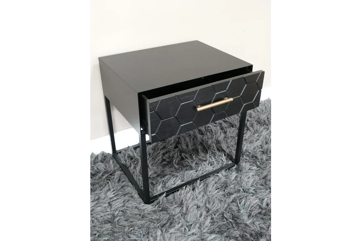 Black bedside table with hexagon drawer front and gold handle on grey rug