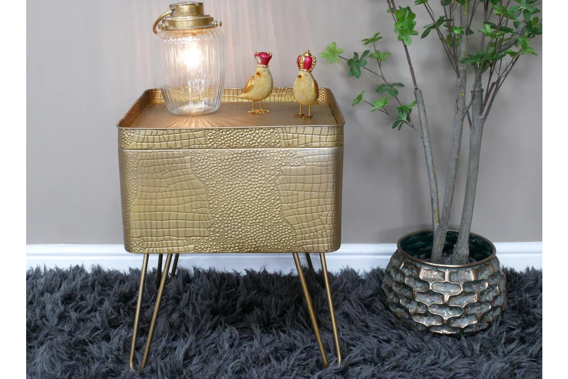 Gold textured side table with hairpin legs, glass lamp, decorative birds, and artificial plant