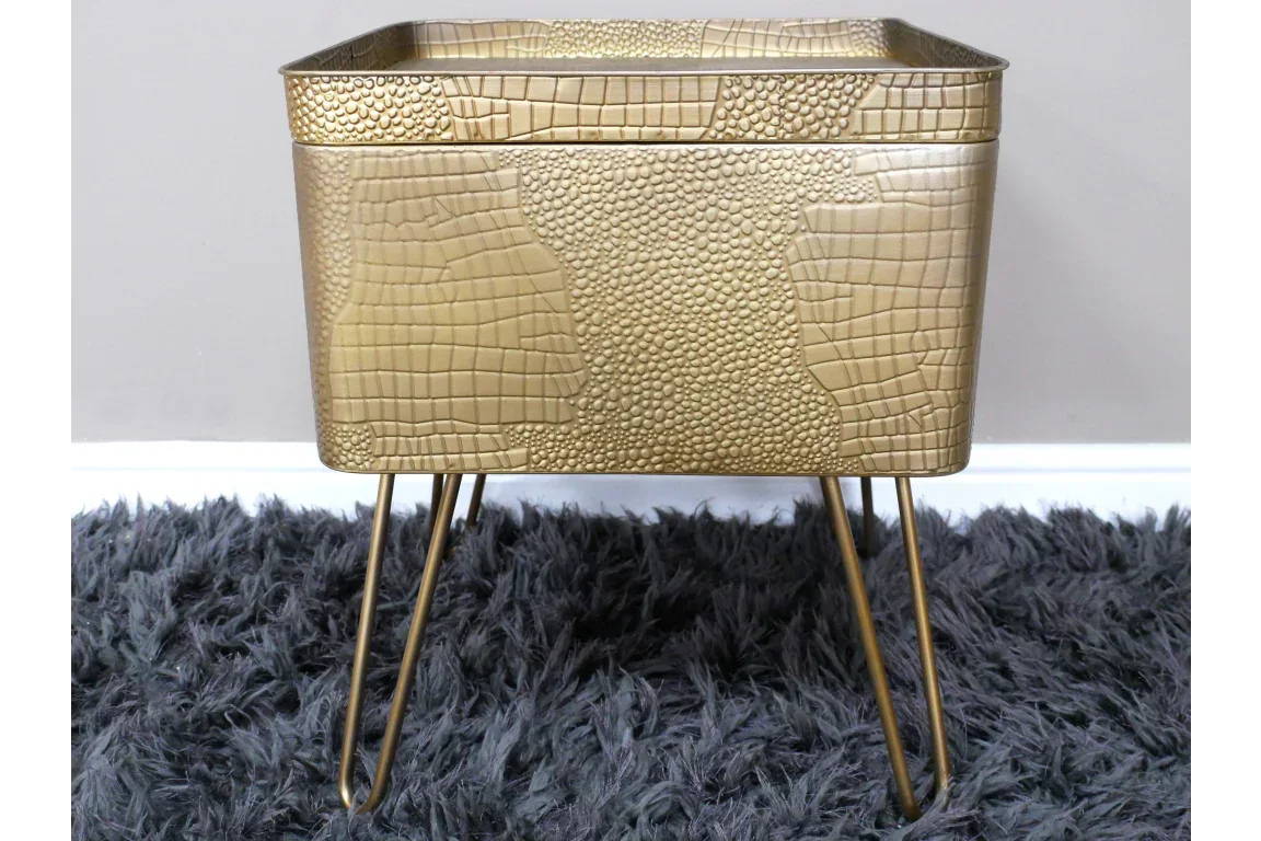 Gold metal planter with textured reptile pattern and hairpin legs on dark rug