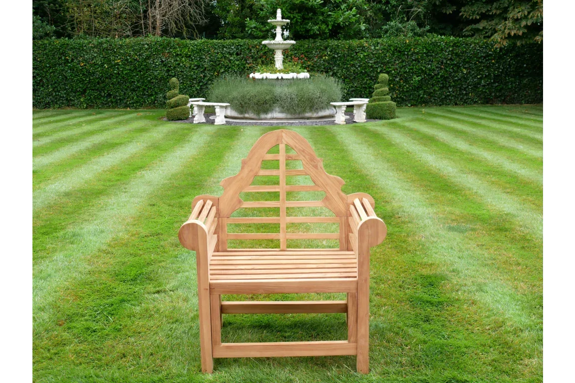 Wooden garden bench with decorative backrest on striped lawn, fountain in background