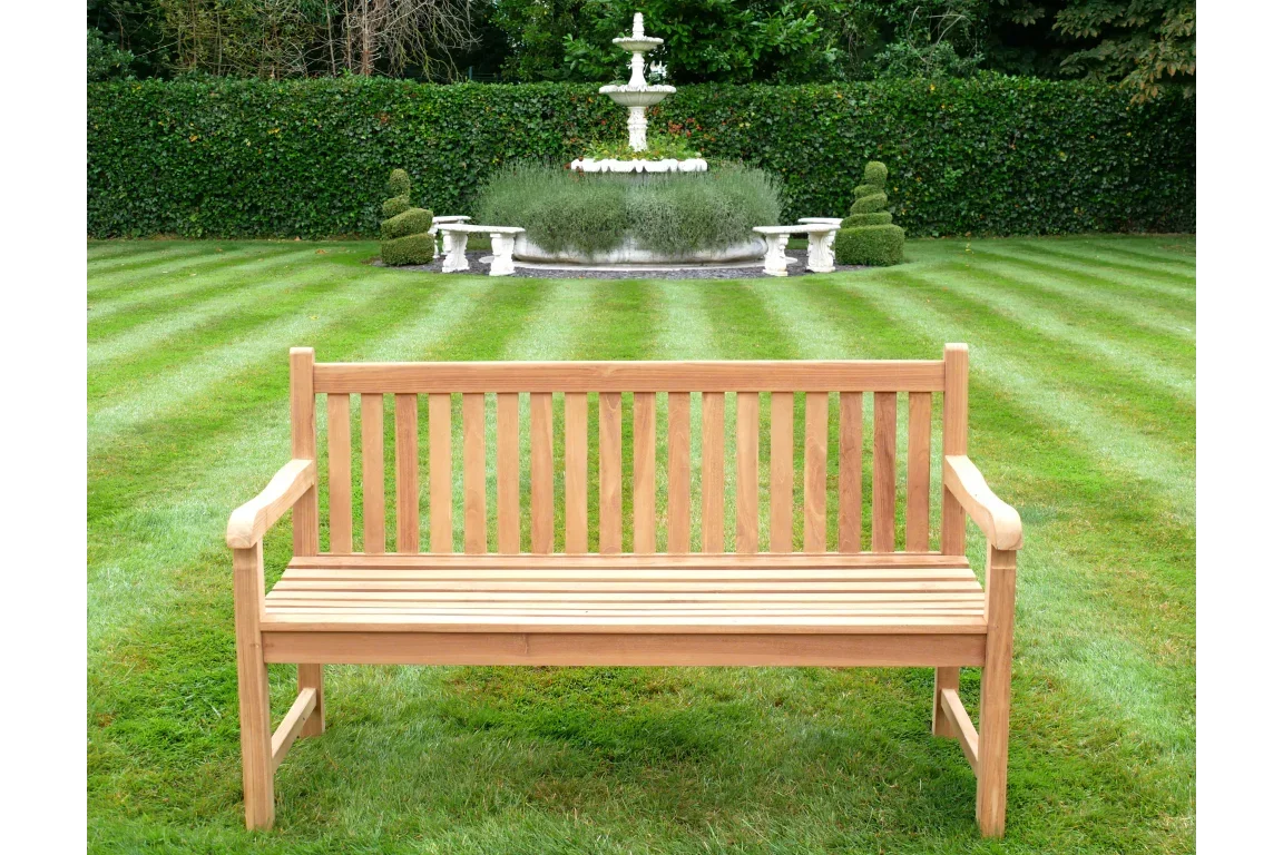 Wooden garden bench with slatted backrest on lawn facing ornamental fountain
