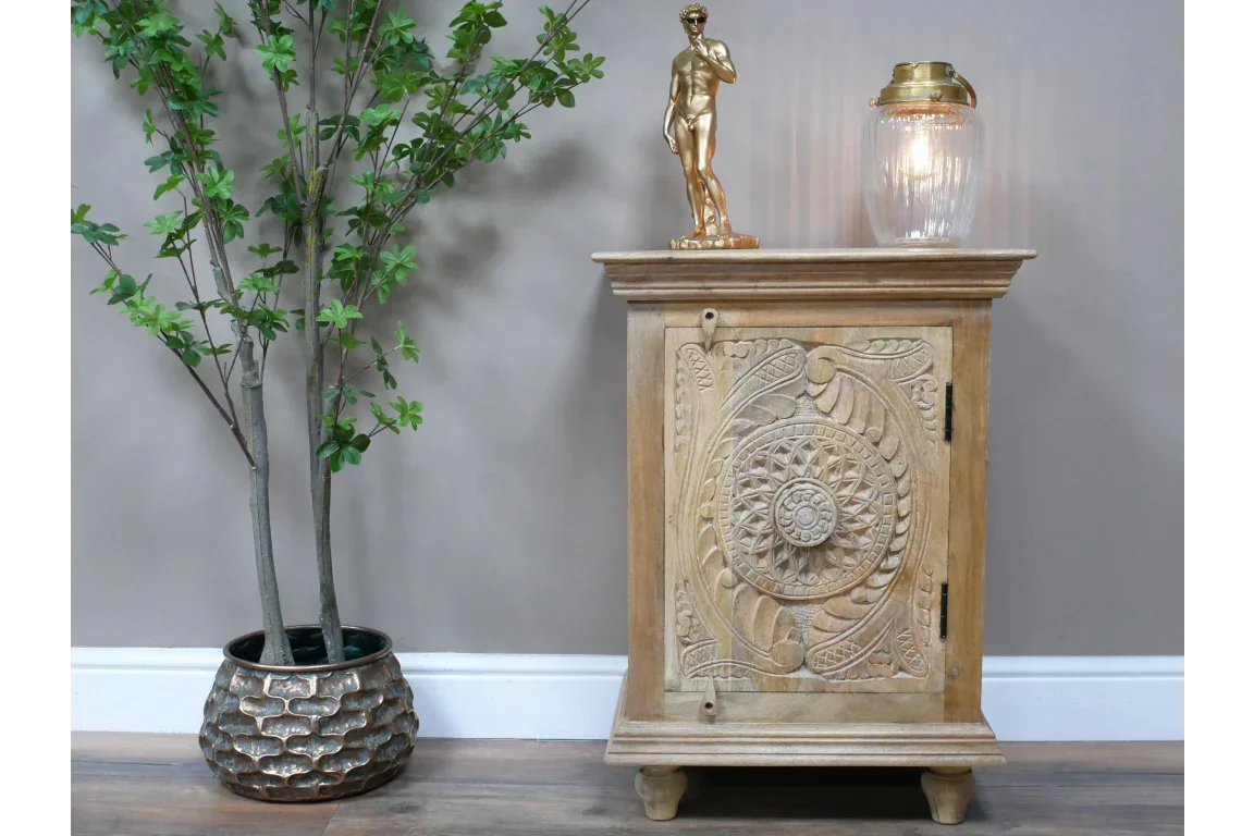 Carved wooden cabinet with ornate front panel beside artificial plant and gold decor accents