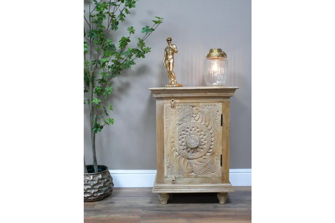 Carved wooden cabinet with ornate door beside potted plant, gold statue and glass lamp on top