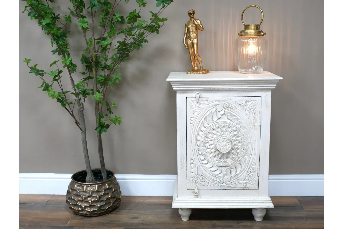 White carved wooden cabinet with ornate door beside potted plant on wooden floor