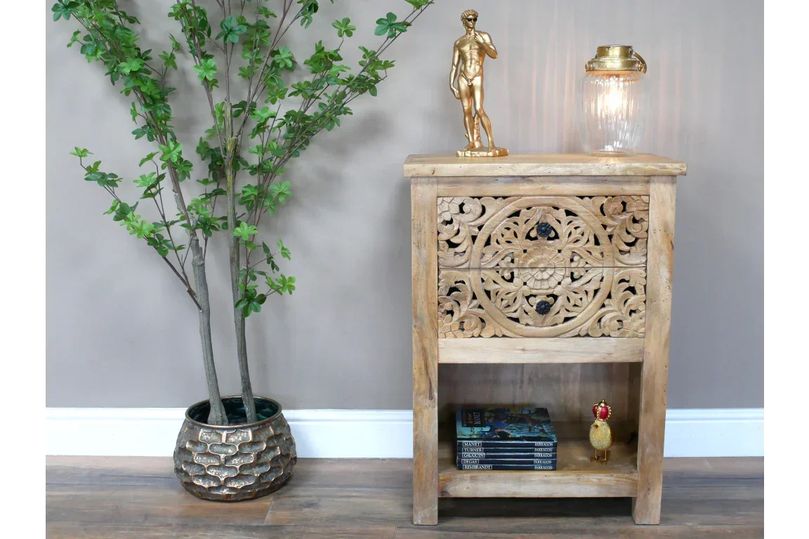 Carved wood side table with decorative front panel, open shelf, books and lamp