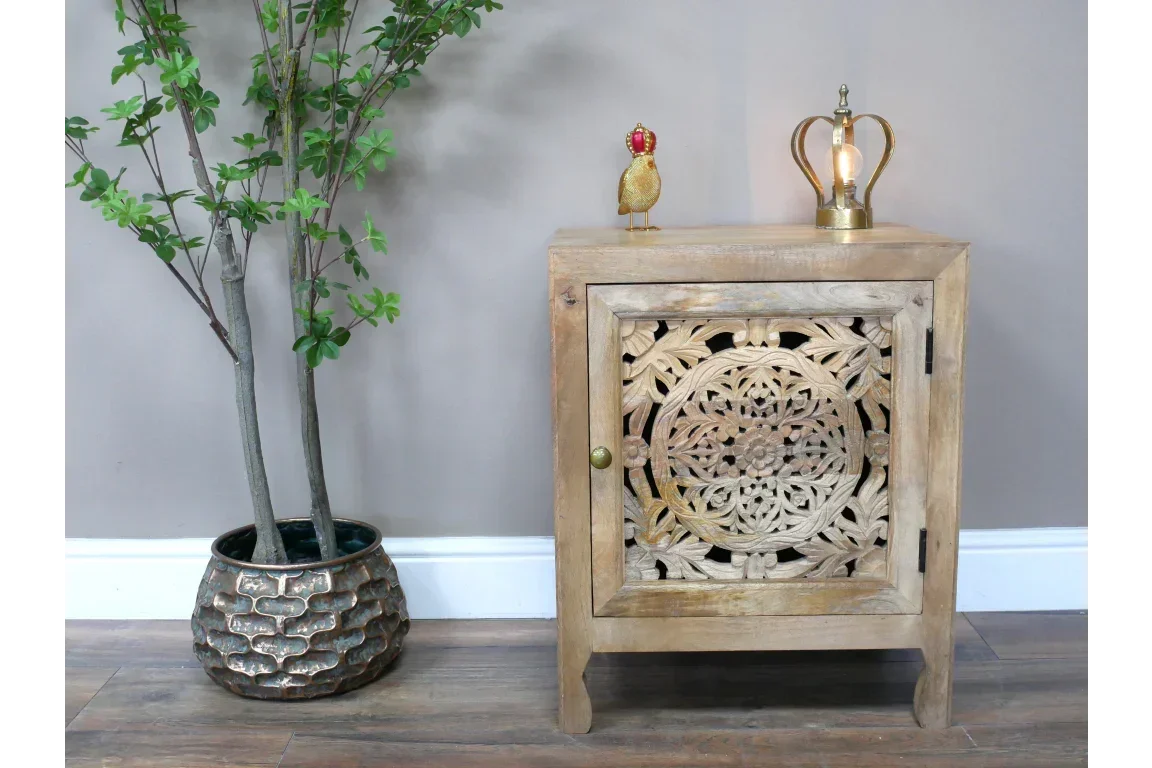 Carved wood bedside cabinet with floral detail beside potted plant on wooden floor