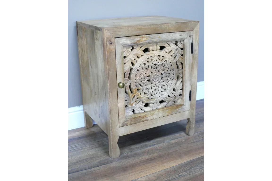 Carved wood bedside cabinet with single ornate door and brass knob on hardwood floor