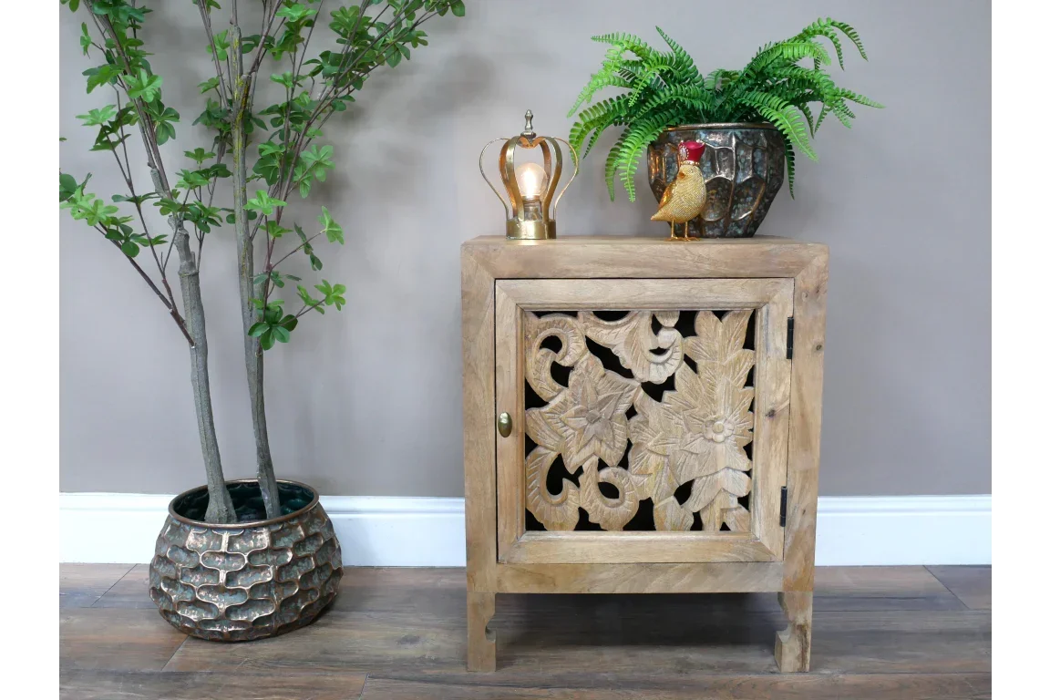 Carved wood side cabinet with floral door pattern, styled with potted fern and decor accents