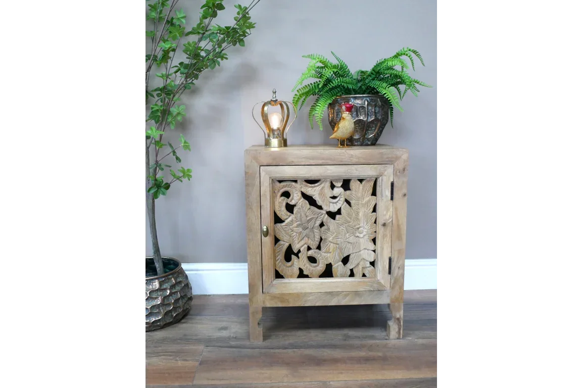 Carved wooden side table with floral door, plant decor, and ornaments on top