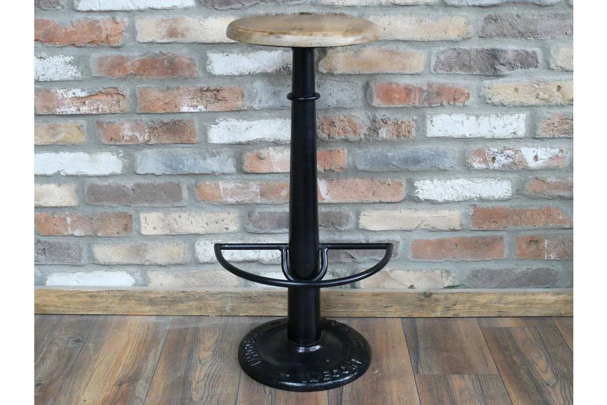 Industrial bar stool with round wooden seat and black metal base against brick wall