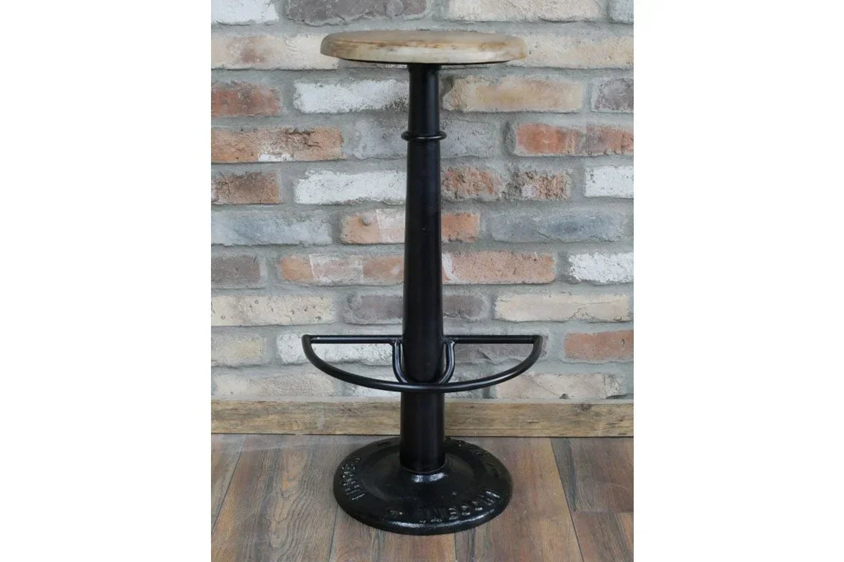 Industrial bar stool with round wooden seat and black metal base against brick wall