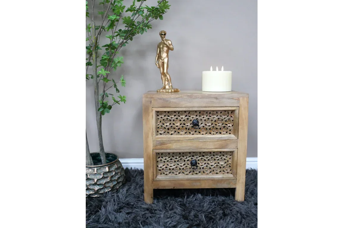 Wooden bedside table with two carved drawers, gold statue, candle, and plant beside