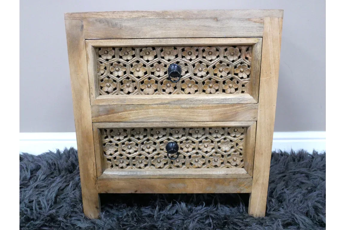 Wooden bedside table with carved floral drawer fronts and black handles on a grey rug