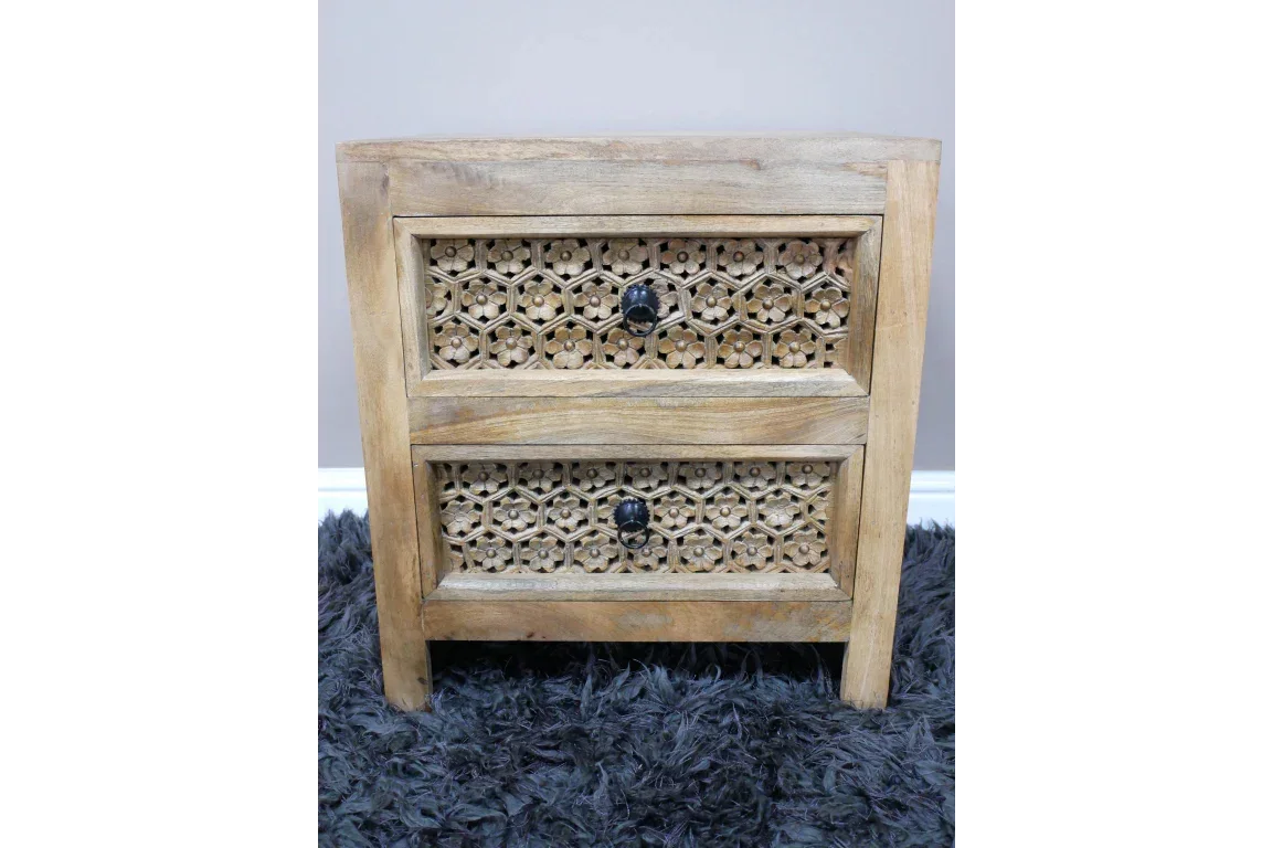 Wooden bedside table with carved floral drawer fronts and black handles on grey rug