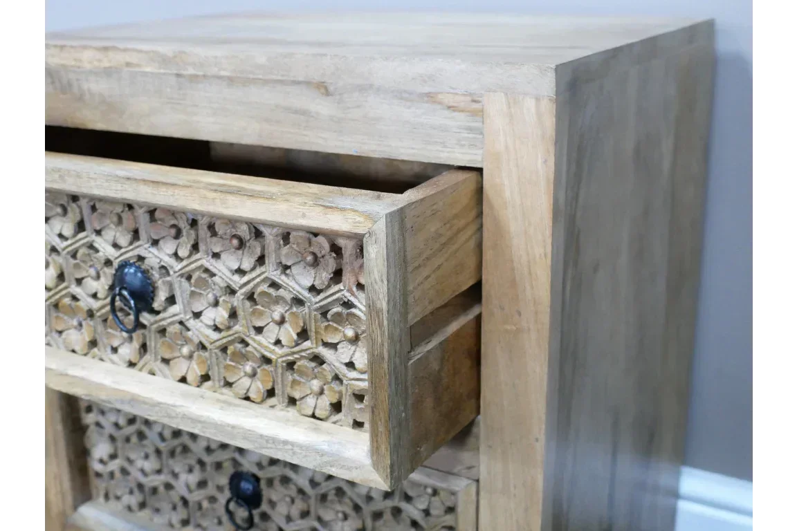 Carved wooden chest of drawers with floral detail and black ring pull handles, angled view