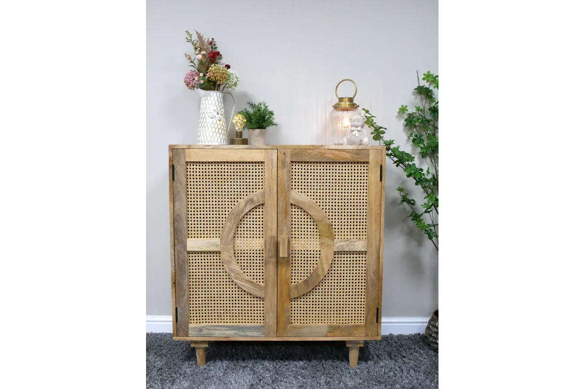 Natural wood sideboard with rattan doors and circular detail, topped with vase and lantern