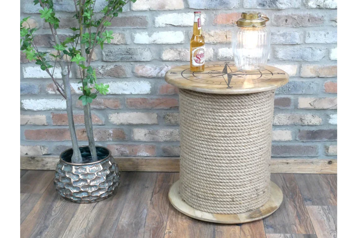 Round rope side table with compass design top beside potted plant on wooden floor