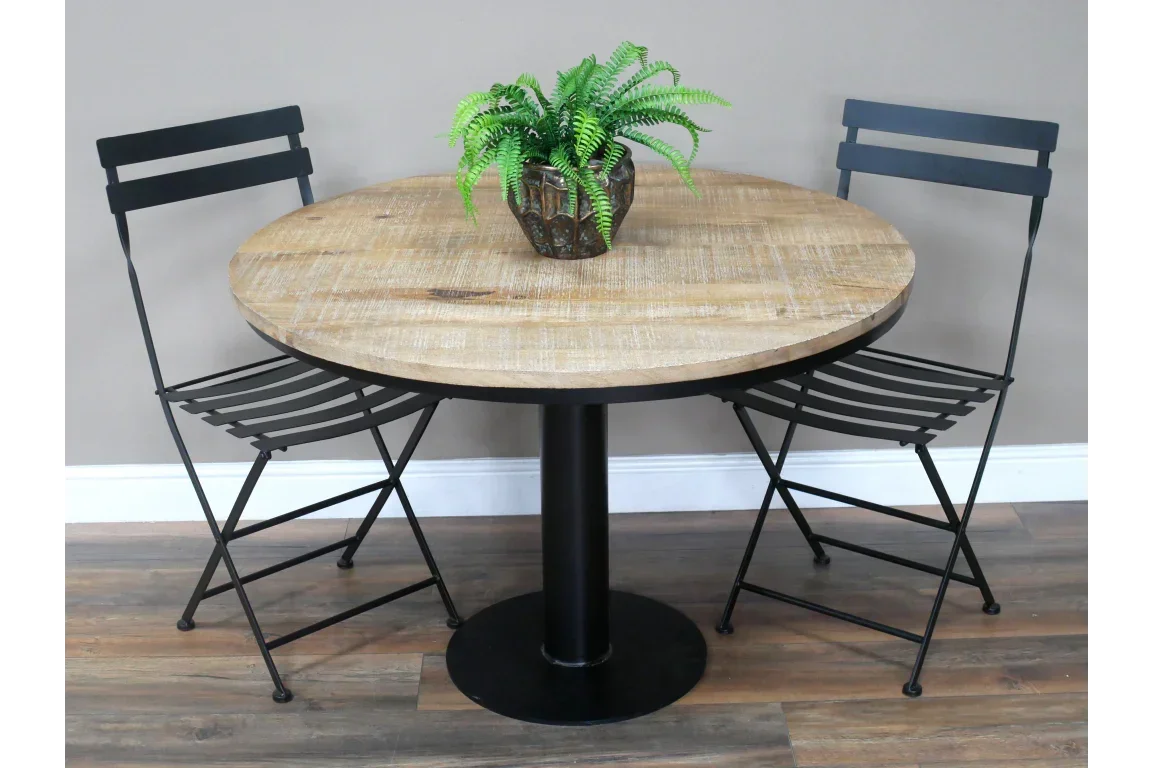 Round wooden dining table with black metal base, two metal chairs, plant centerpiece