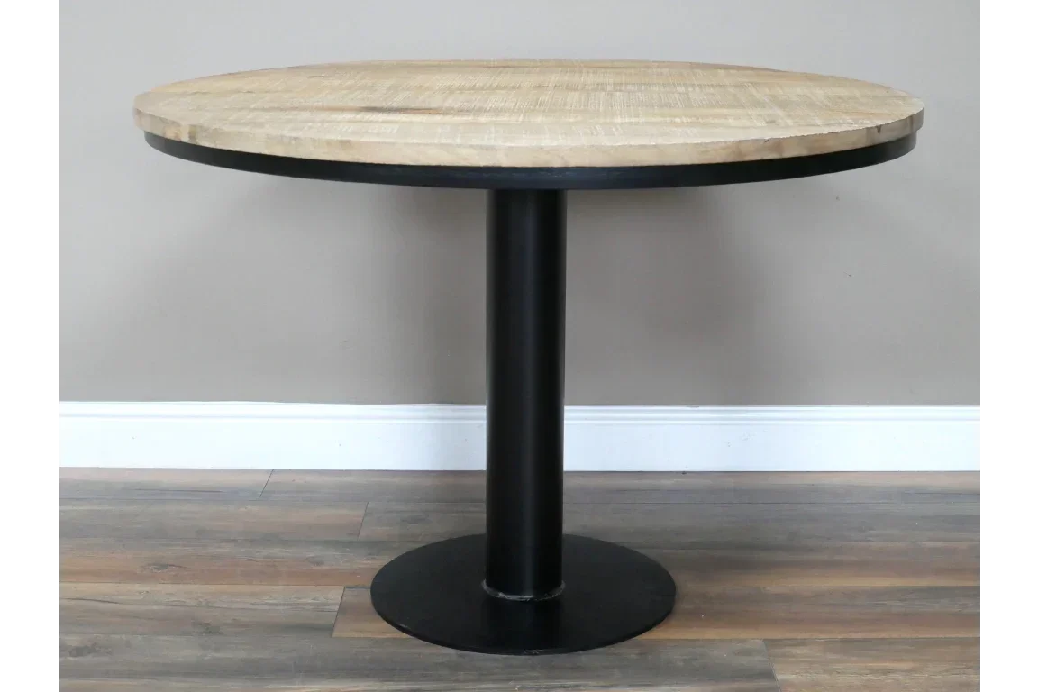 Round wooden dining table with black metal pedestal base on wood floor