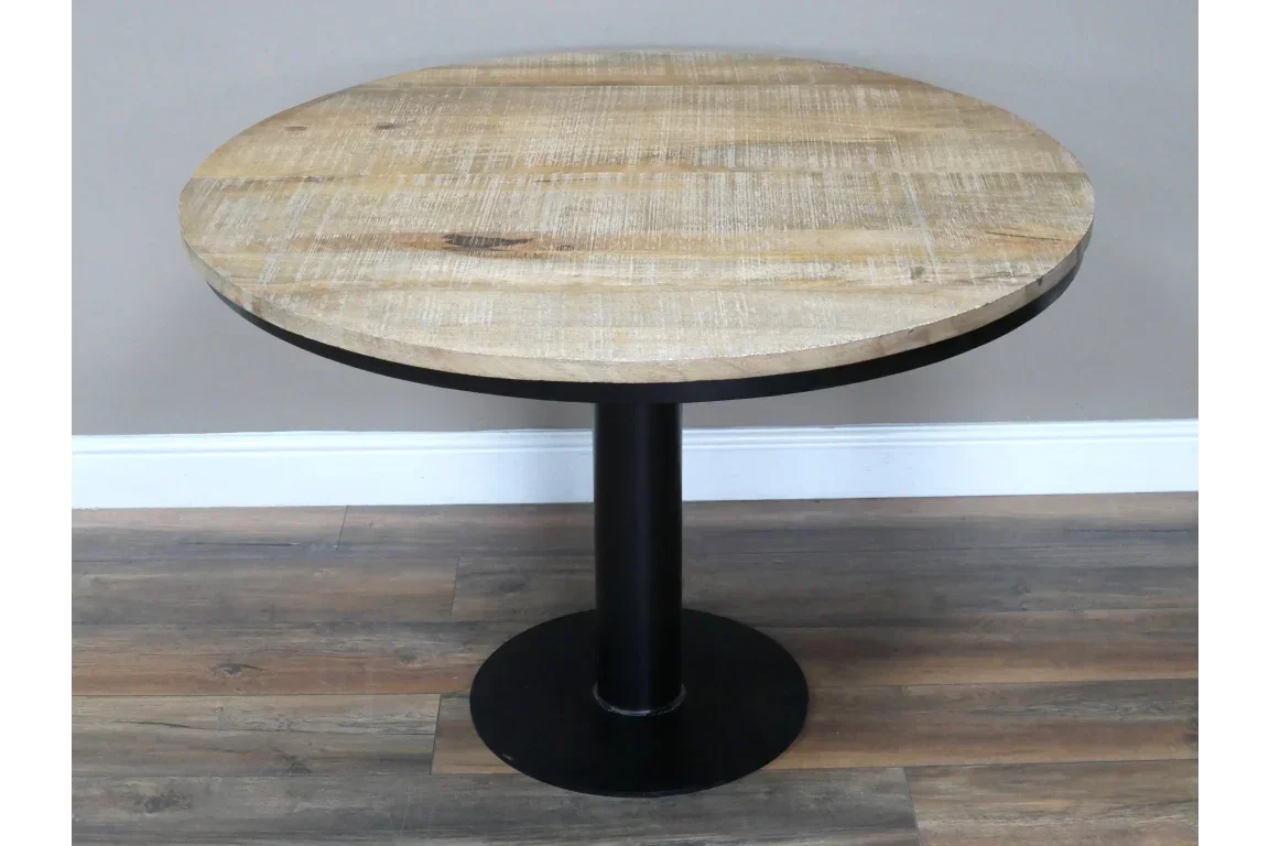 Round wooden dining table with black pedestal base on wood floor