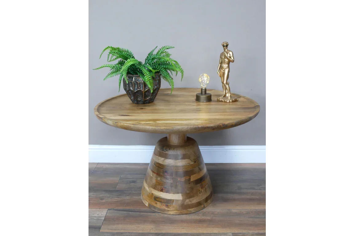 Round wooden dining table with pedestal base, plant pot, lamp, and gold statue on top