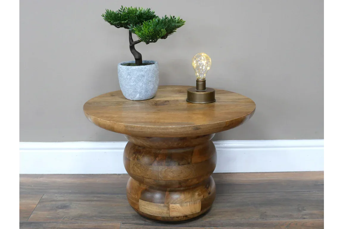 Round wooden side table with sculpted base, potted plant and lamp on top