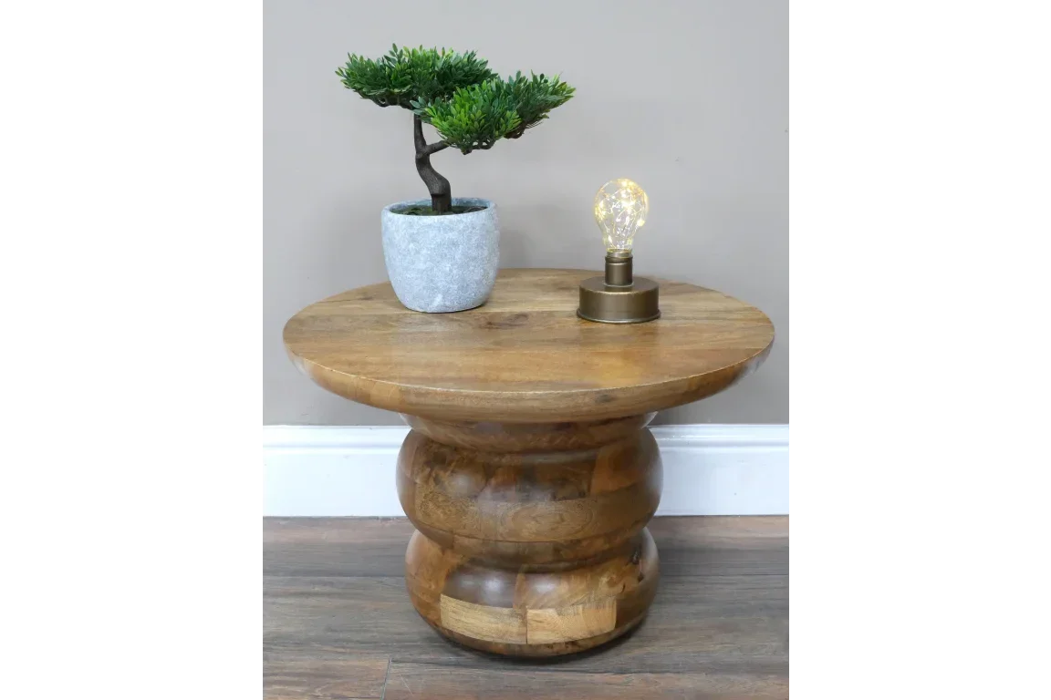 Round solid wood side table with turned base, potted plant and small lamp on top