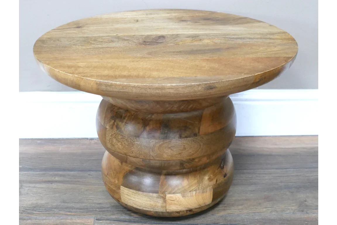 Round solid wood side table with natural finish and sculpted base on wooden floor