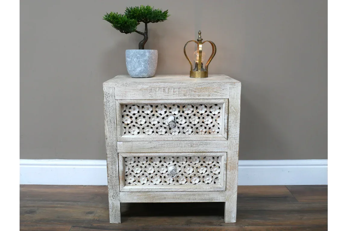 Wooden bedside table with carved floral drawer fronts and decorative top accessories