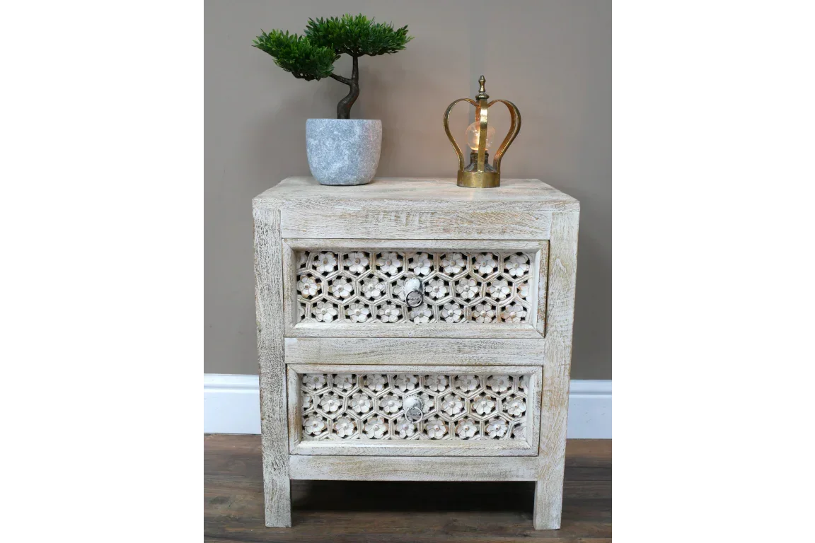 Wooden bedside table with carved floral drawers, plant and lamp on top