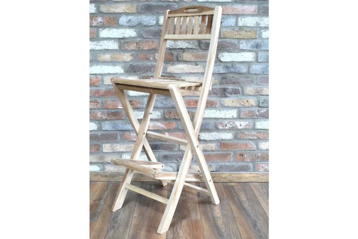 Folding wooden bar stool with slatted backrest on wood floor against brick wall