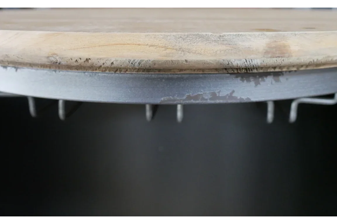 Closeup of round wood table edge with grey metal frame and hooks underneath