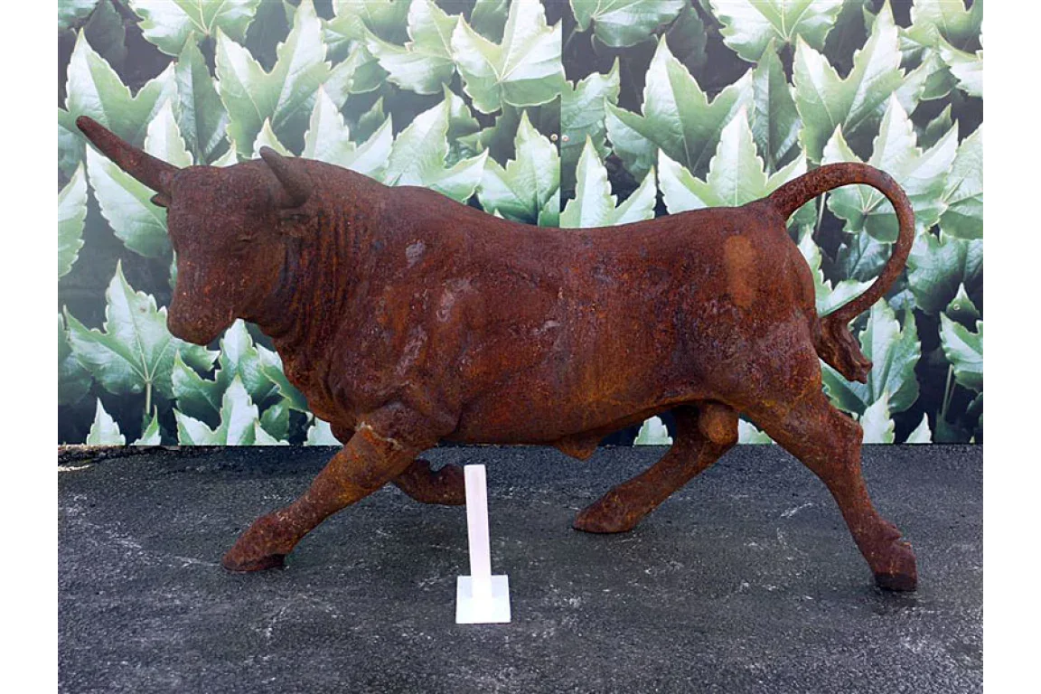 Rust effect bull garden sculpture on outdoor surface with leaf mural background