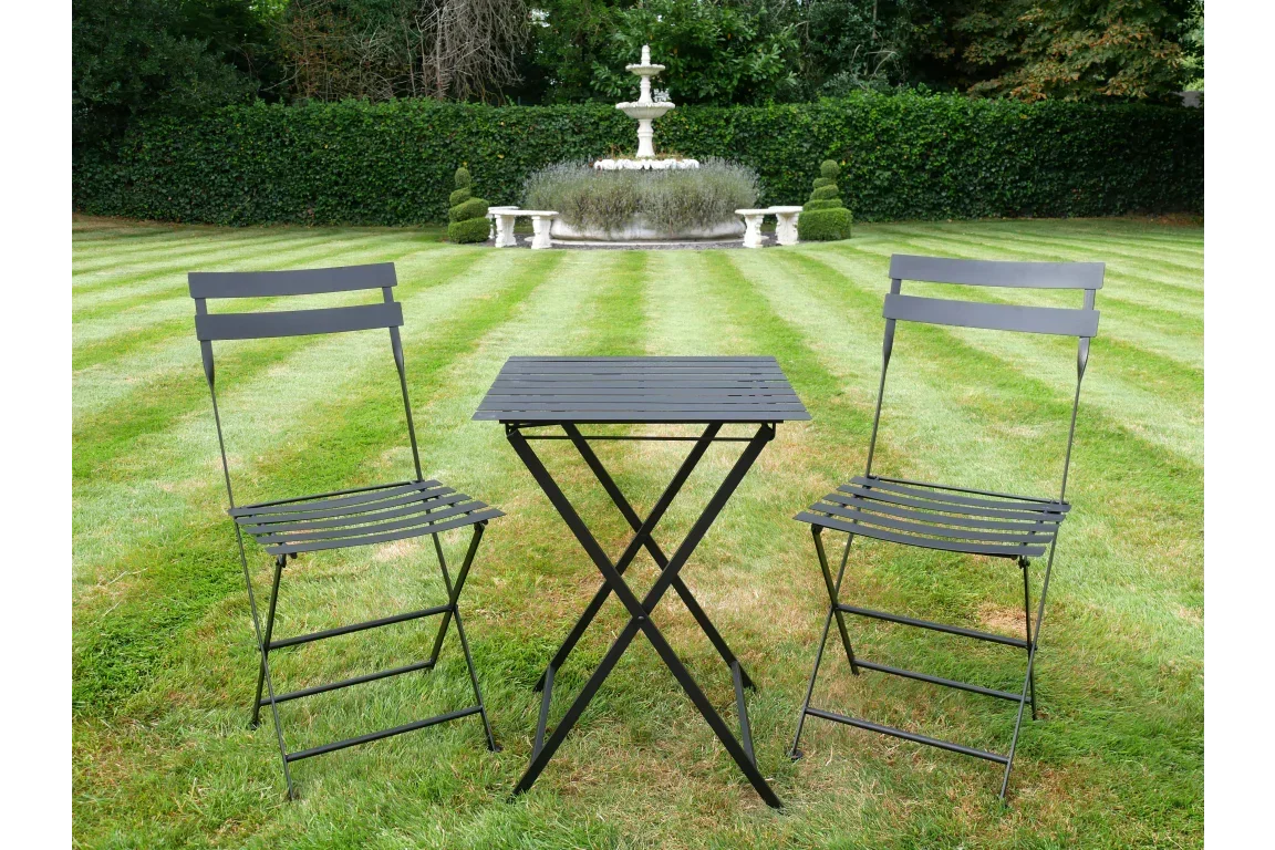 Black metal bistro set with two chairs and table on lawn, garden fountain in background
