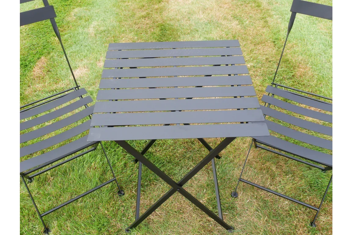 Black metal bistro table and two chairs set on grass, slatted design, outdoor furniture