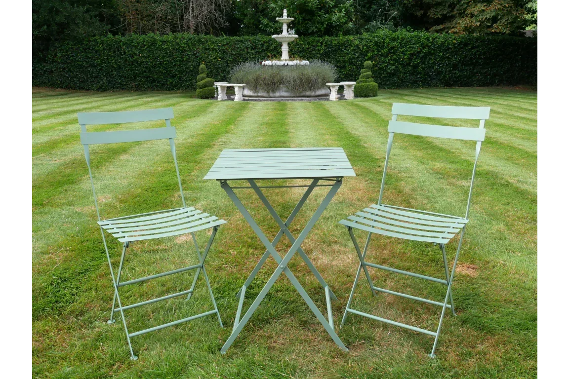 Light green metal bistro set with two chairs and square table on garden lawn