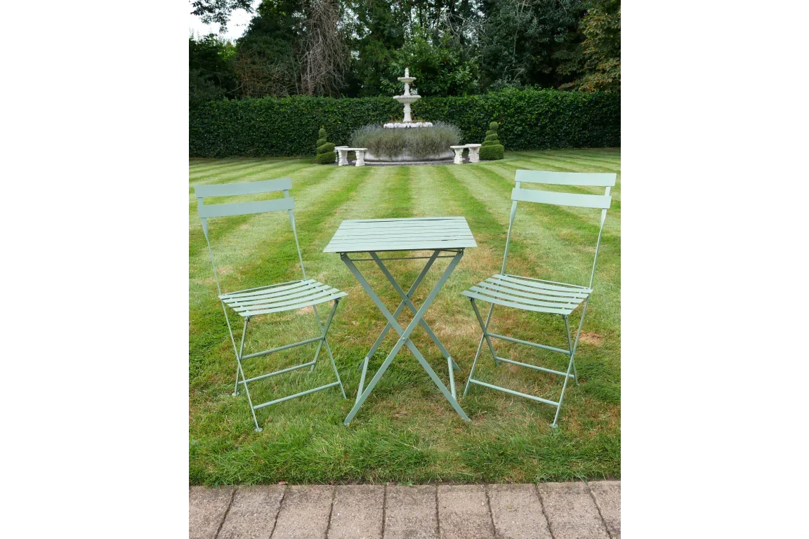 Green metal bistro set with two chairs and square table on lawn in front of garden fountain