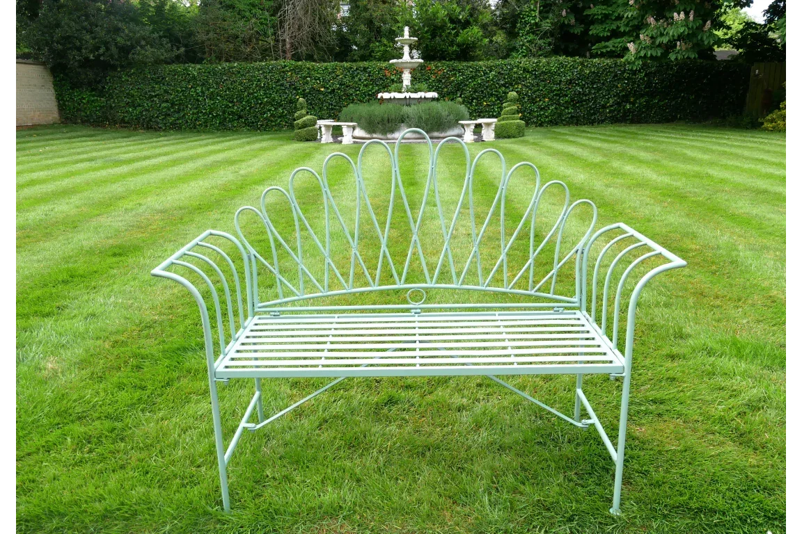 Light green metal garden bench with decorative backrest on a striped lawn