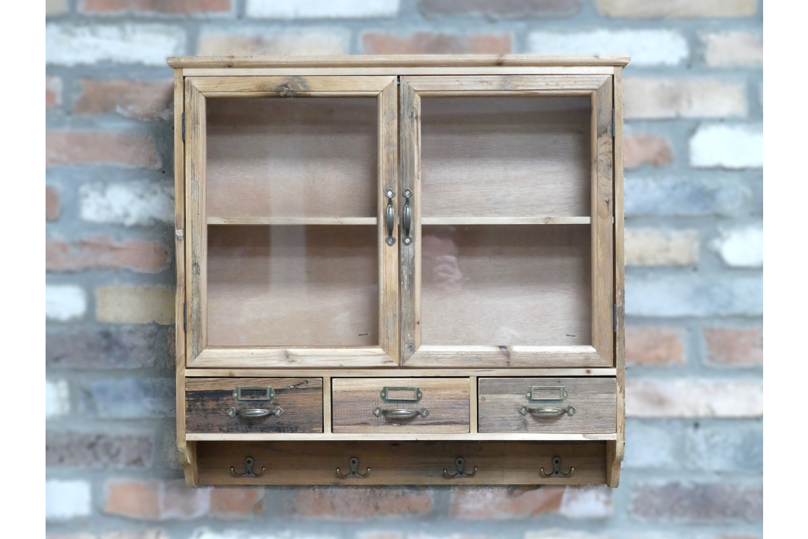 Wooden wall unit with two glass-front doors, three drawers, and four metal hooks, shown mounted on brick wall.
