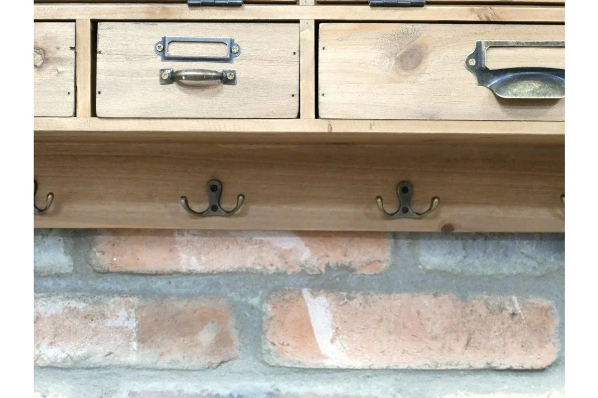 Wooden wall mounted coat rack with metal hooks and small drawers against brick wall