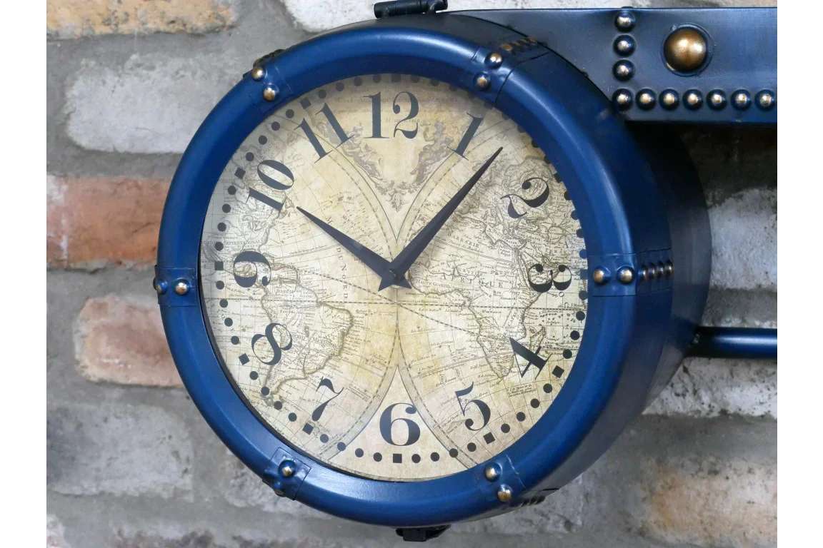 Blue vintage wall clock with world map face and black numerals mounted on stone wall