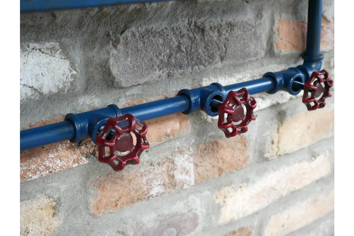 Industrial style blue metal pipe coat rack with red valve hooks on brick wall