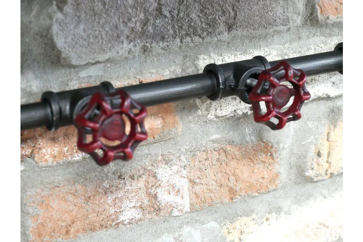 Industrial pipe coat hooks with red metal valve handles mounted on exposed brick wall