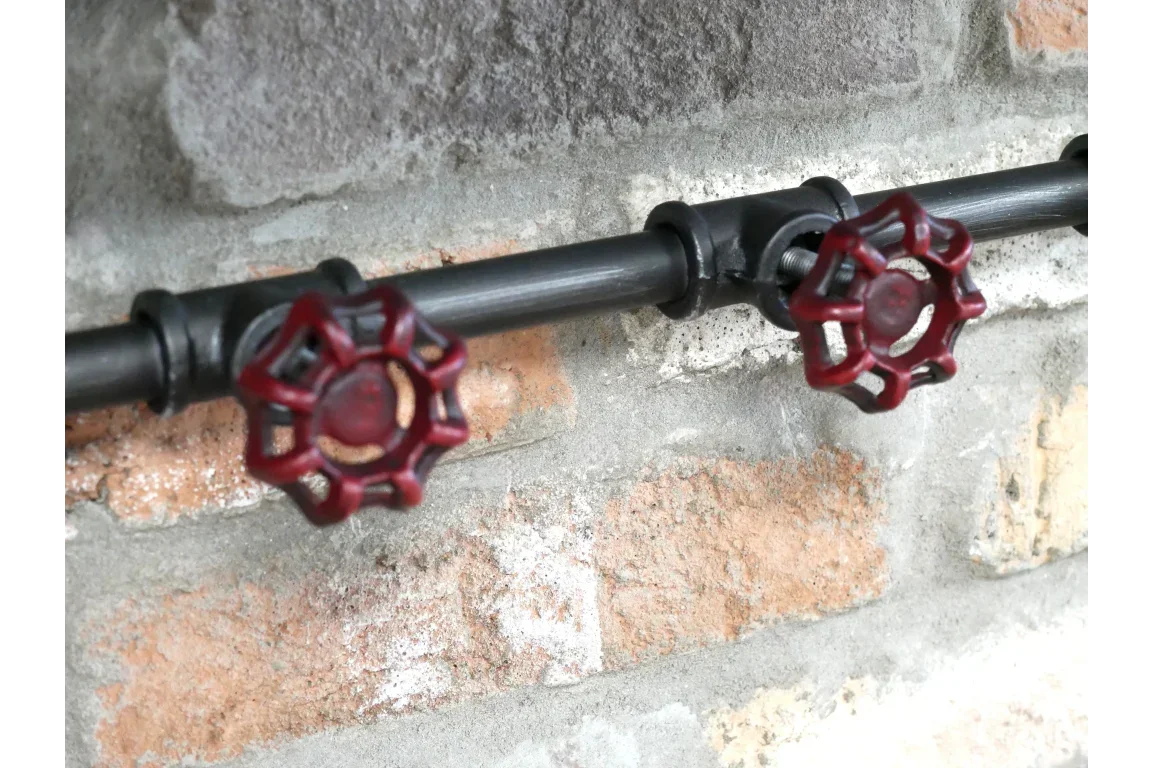 Industrial black metal pipe handle with two red valve grips mounted on brick wall