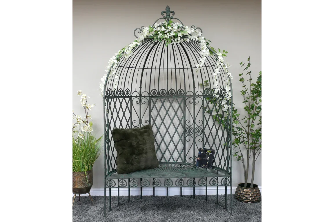 ornate metal garden bench with domed trellis surround, green cushion, and floral garland accent