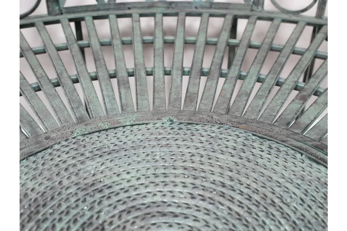 Closeup of metal garden chair seat with green patina and woven pattern