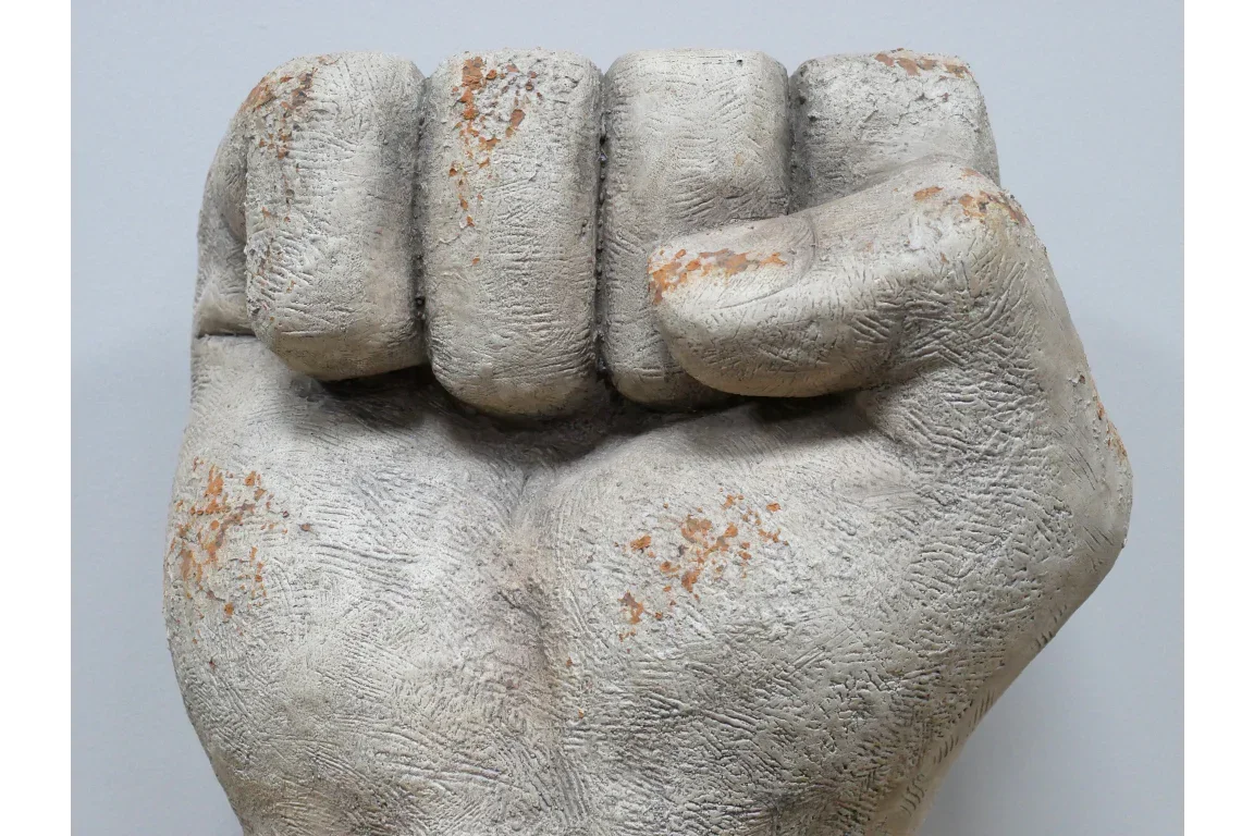 Textured concrete fist sculpture with weathered finish and visible rust details