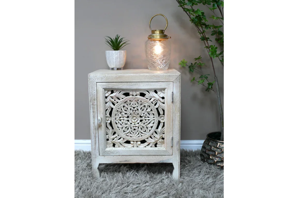 Carved wood side table with whitewash finish, plant, and lantern on top, indoor setting